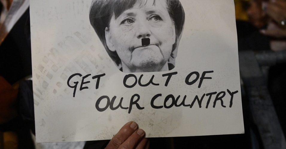 19.mar.13 - Manifestante segura cartaz com a foto da chanceler da Alemanha, Angela Merkel, com um bigode semelhante ao do nazista Adolf Hitler, em protesto em Nicósia, no Chipre. No cartaz está escrito ?Saia do nosso país?