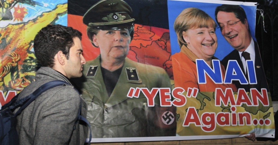 27.mar.13 - Homem passa em frente a faixa contra Angela Merkel em frente ao palácio presidencial de Nicósia, no Chipre