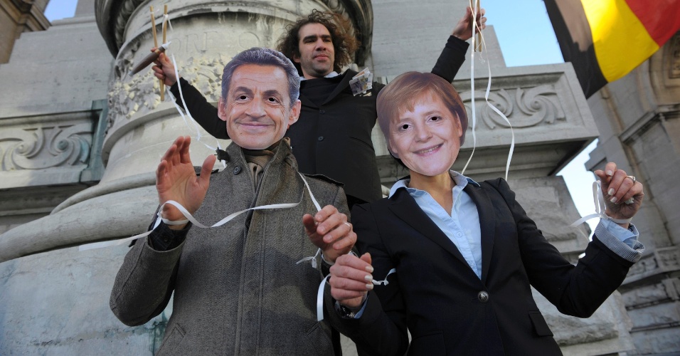 9.dez.11 - Manifestante simula movimentar dois bonecos de fantoche, que são outros manifestantes com as máscaras do então presidente da França, Nicolas Sarkozy, e da chanceler alemã, Angela Merkel, em protesto durante a reunião do conselho europeu, em Bruxelas, Bélgica. A dupla de políticos defensores de cortes nos orçamentos públicos foi apelidada de "Merkozy"