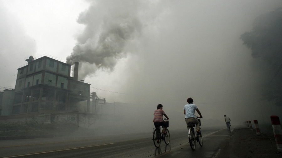 O aquecimento global é provocado pela emissão de gases como CO2 e metano. Ciclistas passam por ruas cobertas por fumaça emitida por indústria em Yutian, a 100 quilômetros de Pequim - Peter Parks/AFP 