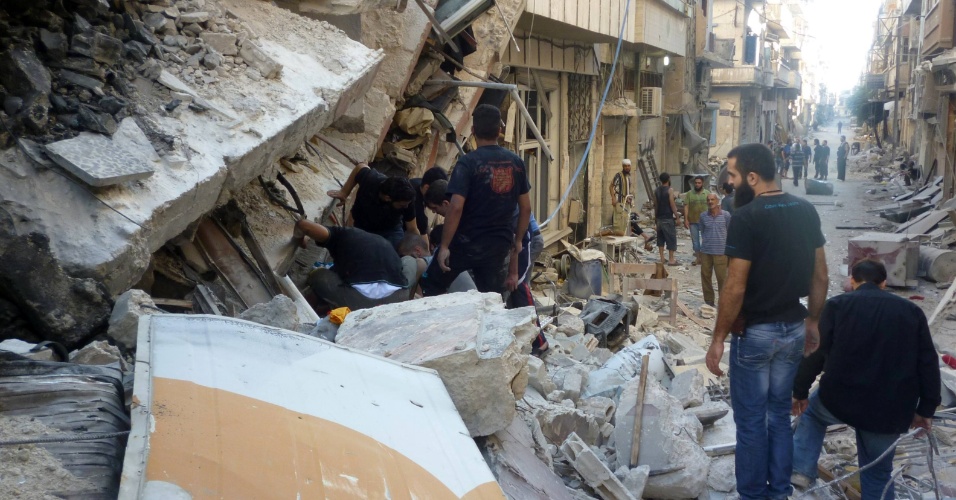 26.jul.2013 - Pessoas buscam por sobreviventes em um local atingido por um ataque de mísseis do regime sírio, na área sitiada de Homs, Síria