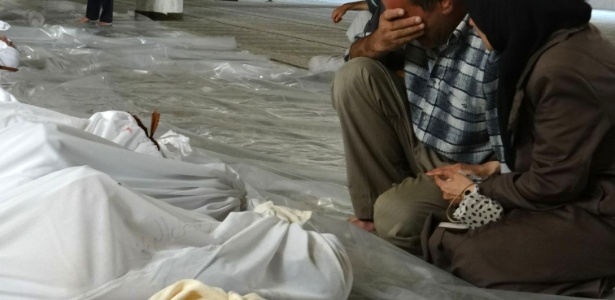 Casal sírio chora em frente de corpos cobertos com lençóis após o que a oposição síria afirmou ser um ataque com gás tóxico disparado por forças do governo de Bashar Al Assad, no leste Ghouta, nos arredores de Damasco, na quarta-feira (21), o que deixou mais de mil mortos, inclusive crianças - Shaam News/AFP