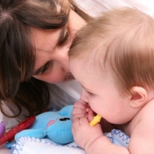Bebê de bruços brinca com a mãe - Thinkstock