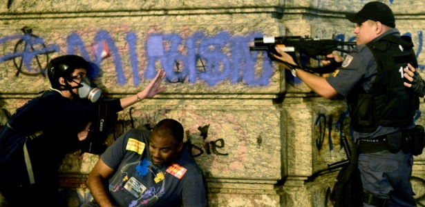 Policial aponta equipamento contra manifestante durante protesto na região central do Rio de Janeiro no Dia do Professor - Yasuyoshi Chiba/AFP