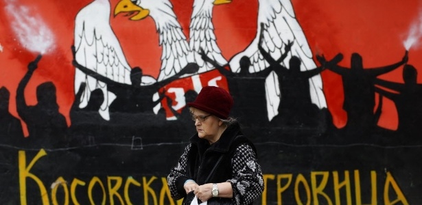 Mulher de origem sérvia passa diante de mural com símbolos da minoria dentro do Kosovo, país que faz sua primeira eleição livre desde a independência, em 2008. A maioria do país é de origem albanesa
