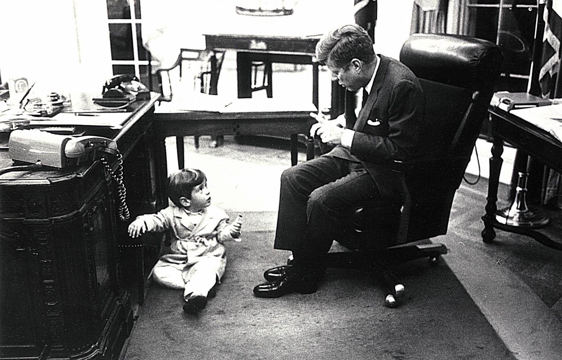 Nesta fotografia de 14 de outubro de 1963, no Salão Oval da Casa Branca, em Washington, Estados Unidos, o presidente norte-americano, John F. Kennedy, brinca com seu filho, John F. Kennedy, Junior. A fotografia foi tirada um mês antes da morte do presidente. **** (FILES) This 14 October 1963 file photo taken in the Oval office of the White House in Washington, DC, shows former US President John F. Kennedy (R) as he speaks with his son John F. Kennedy jr. - AFP