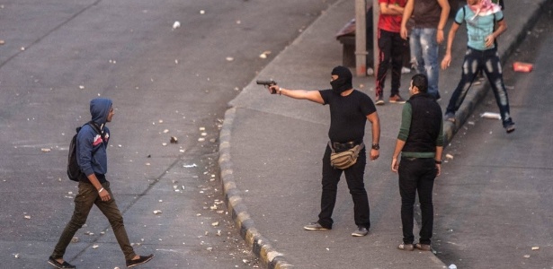 Um homem mascarado aponta sua arma, na companhia de outros colegas que protestam contra os militares, durante o aniversário dos protestos iniciados em 2011, nesta terça-feira (19), nas proximidades da praça Tahir, no Cairo - Mahmoud Khaled/AFP