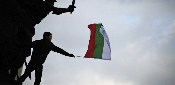 Estudante segura bandeira búlgara após subir em monumento durante protesto contra o governo - Vassil Donev/Efe