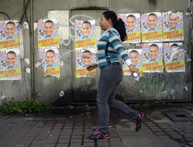 Mulher passa por cartazes da candidatura de Ernesto Villegas, do partido Socialista, à Prefeitura de Caracas. Villegas é ex-ministro das comunicações e tem o apoio do presidente Nicolas Maduro - Leo Ramirez/AFP