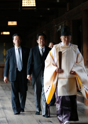 O primeiro-ministro do Japão, Shinzo Abe, acompanhado por segurança, é conduzido por sacerdote xintoísta, em visita ao santuário