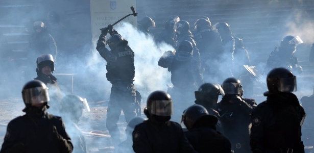 Em Kiev, policiais cortam madeira, enquanto outros se posicionam em frente a manifestantes - Sergei Supinsky/AFP