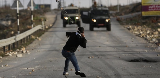 Manifestante palestino utiliza estilingue contra veículos do Exército de Israel em Jalazoun, nas proximidades de Ramallah - Darren Whiteside/Reuters