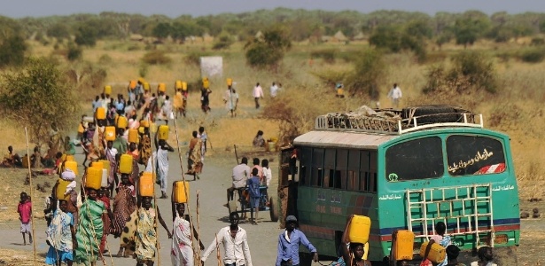 Pessoas deslocadas internamente (PDIs) carregam água enquanto caminham em direção à entrada de uma missão das Nações Unidas na República do Sudão do Sul (UNMISS), com base em Malakal, nesta quinta-feira (6). Em seus combates recentes, o país tem visto ondas de ataques de vingança brutal, como lutadores e milícia étnica usando a violência para saquear e acertar velhas contas. As Nações Unidas e os ativistas de direitos humanos têm relatado que atrocidades horríveis foram cometidas por ambos os lados - AFP/Carl de Souza