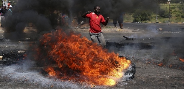 Manifestante reage na frente das chamas de um pneu queimado enquanto participa de um protesto por melhores serviços públicos em Mabopane, província ao norte de Pretória, na África do Sul, na sexta-feira (7) - Siphiwe Sibeko/Reuters