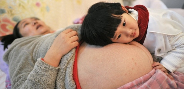 A chinesa Li Yan aguarda para ser examinada, enquanto sua filha apoia a cabeça em sua barriga - China Daily/Reuters