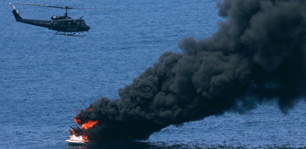 Helicóptero da polícia sobrevoa barco que pegou fogo no mar, próximo ao posto sete da Barra da Tijuca - Ricardo Moraes/Reuters