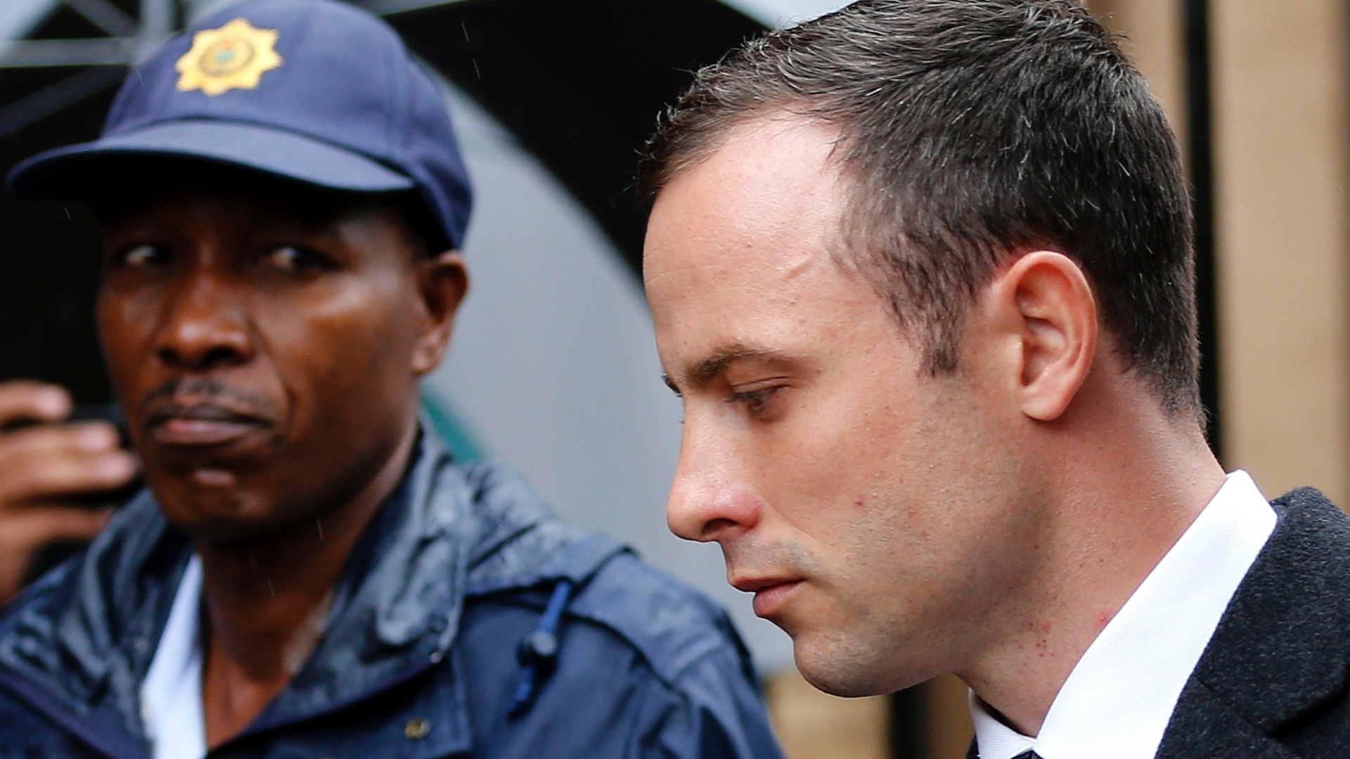 7.mar.2014 - Policial observa o atleta paraolímpico sul-africano Oscar Pistorius chegar ao tribunal em Pretória para o quinto dia de seu julgamento pelo assassinato de sua namorada, Reeva Steenkamp