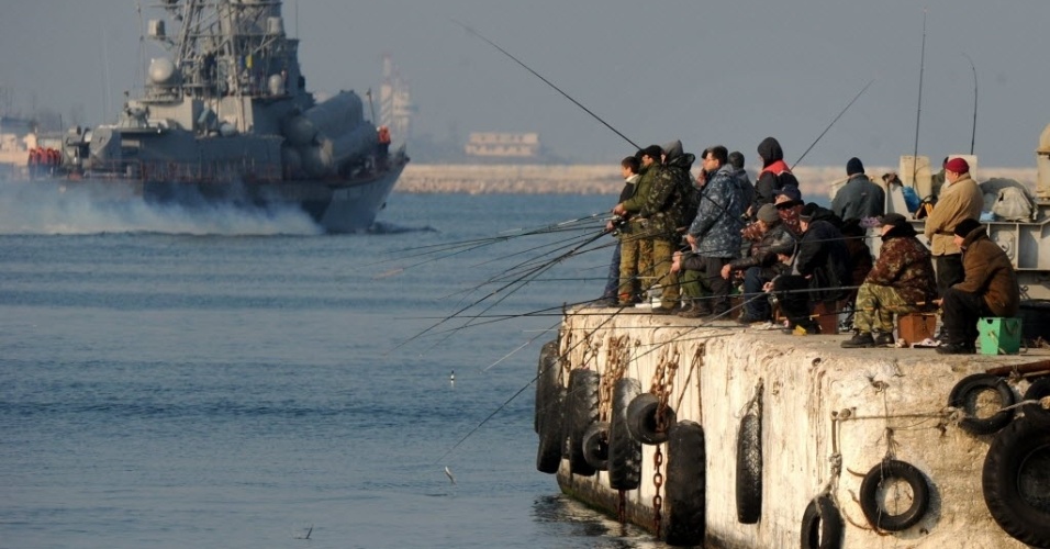 12.mar.2014 - Pessoas pescam em um cais próximo a uma embarcação naval russa em Sebastopol