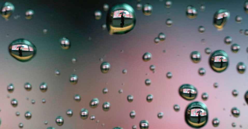 3.abr.2014 - Gotas da chuva em vidro de automóvel mostram uma pessoa com guarda-chuva caminhando perto painel da bolsa de valores, em Tóquio, no Japão, nesta quinta-feira (3)