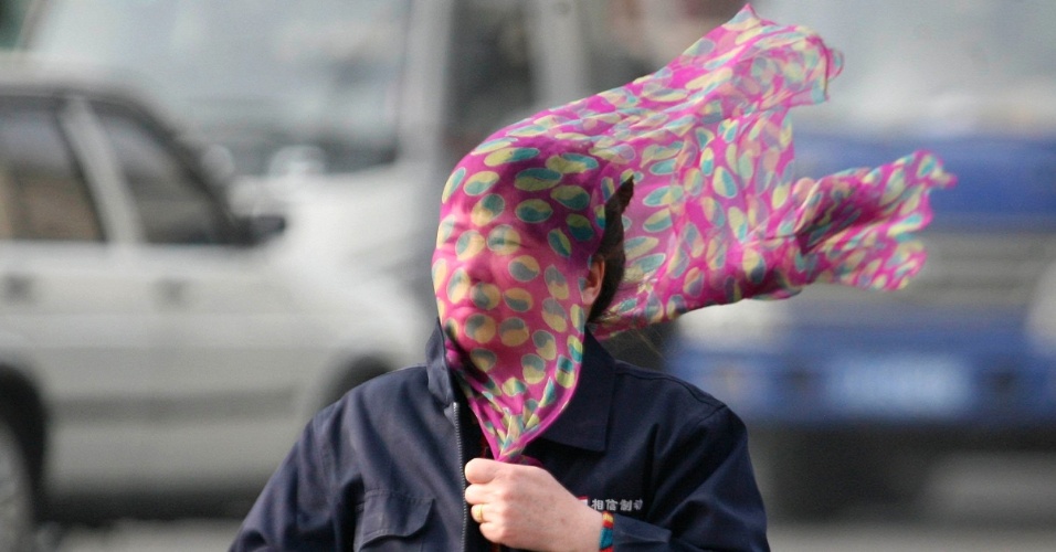 14.abr.2014 - Mulher cobre o rosto com um lenço enquando atravessa uma rua em meio a forte vento em Shenyang, província de Liaoning, na China