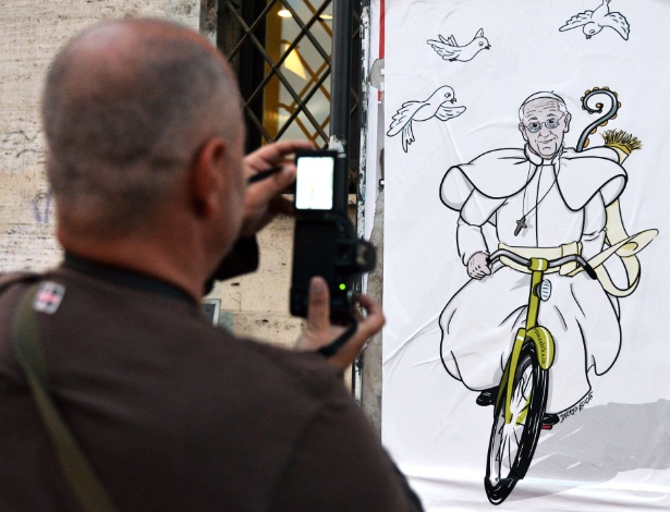14.abr.2014 - Um turista tira foto de um cartaz que traz desenho no qual o papa Francisco aparece andando de bicicleta, em rua de Roma - Vincenzo Pinto/AFP