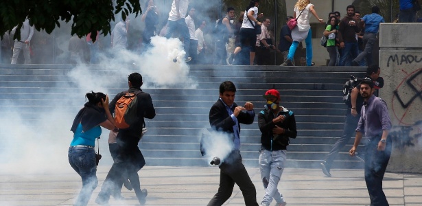 Venezuelanos fogem de bombas de gás lacrimogêneo lançadas durante confronto entre policiais e manifestantes anti-governo, em Caracas - Carlos Garcia Rawlins/Reuters