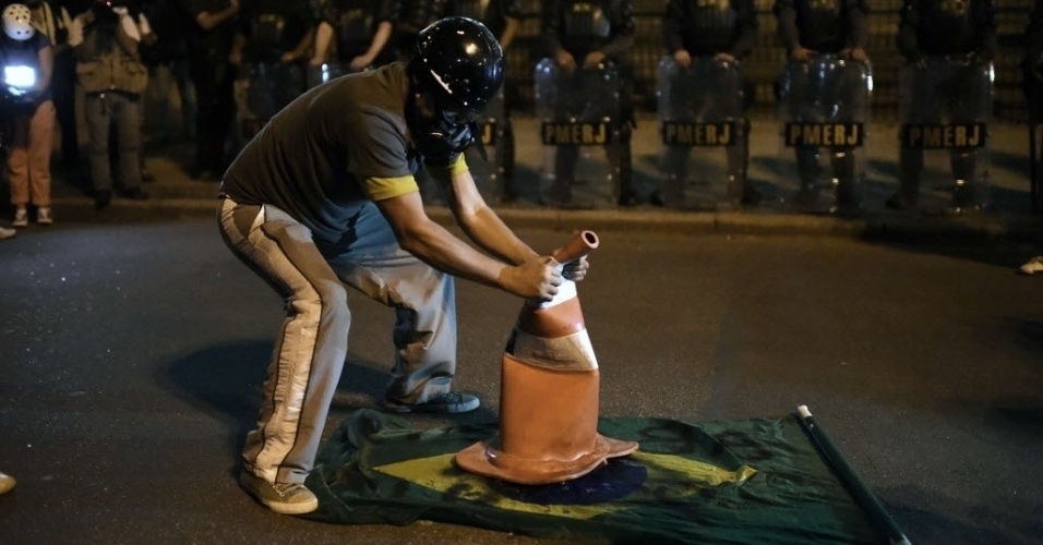 15.mai.2014 - Manifestante coloca cone sobre bandeira do Brasil, enquanto é observado por policiais militares, durante protesto contra a Copa do Mundo no Rio de Janeiro, nesta quinta-feira (15)