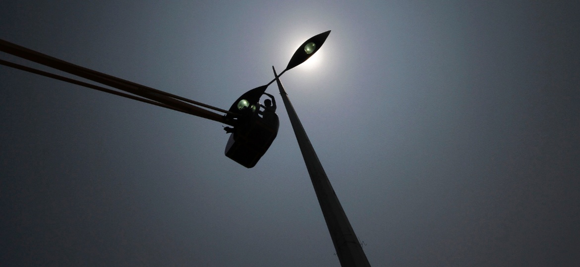 Trabalhador em silhueta contra o sol enquanto instala uma luz de rua em um dia quente na cidade de Chennai, na Índia - Babu/Reuters