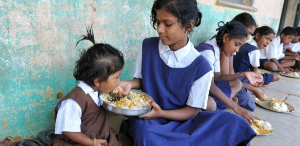 Estudante alimenta irmã mais nova durante almoço em escola primária de Hyderabad, na Índia