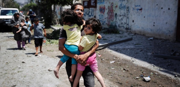 Palestino carrega criança enquanto foge de ataque na faixa de Gaza - Finbarr O"Reilly/Reuters