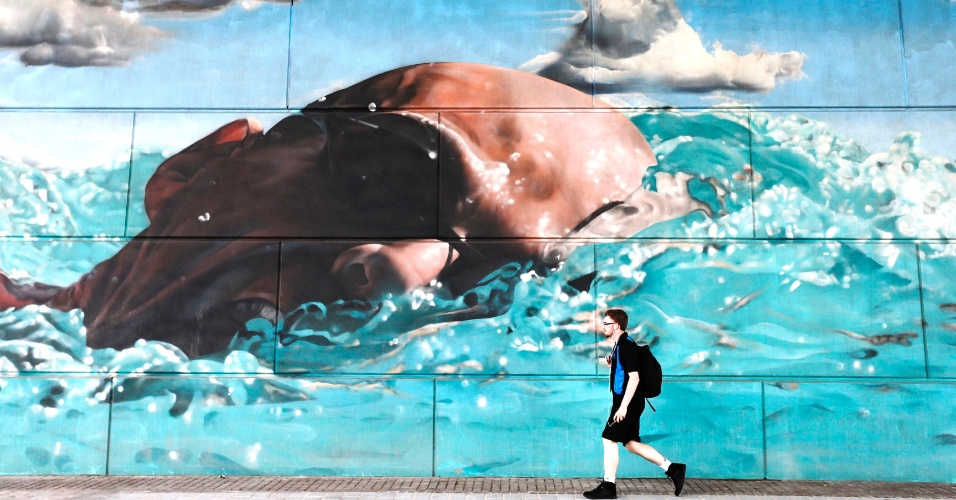 22.jul.2014 - Pedestre passa por mural de nadador competindo próximo de local dos jogos da Commonwealth em Glasgow, no Reino Unido