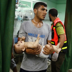 Homem carrega bebê em hospital após ataque de Israel contra escola da ONU matar 16 e ferir ao menos 200 em Gaza - Por Nidal al-Mughrabi e Allyn Fisher-Ilan