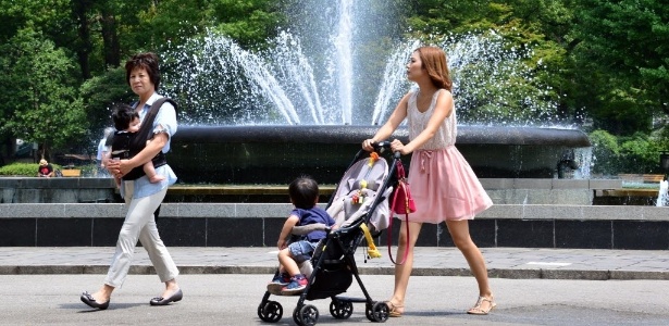 Mães com seus filhos passam por uma fonte de água em parque de Tóquio. O forte calor do verão no Japão já deixou ao menos 15 mortos - Yoshikazu Tsuno/AFP