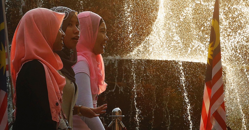 1º.ago.2014 - Mulheres passam junto de bandeiras nacionais da Malásia em Kuala Lumpur durante o feriado de Eid al-Fitr