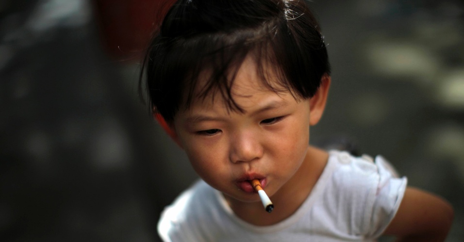 1º.ago.2014 - Criança pega cigarro apagado do chão e põe na boca em uma calçada em Xangai, na China