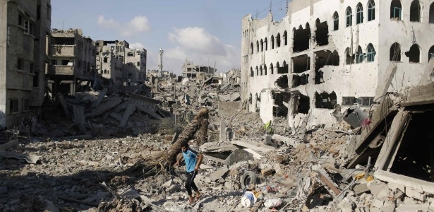 4.ago.2014 - Palestino caminha em meio aos escombros no bairro de Shejaia, que, segundo testemunhas, foi fortemente atingido por ataques e bombardeios aéreos israelenses durante uma ofensiva no leste da Cidade de Gaza. A reconstrução das áreas danificadas em Gaza custará pelo menos US$ 6 bilhões