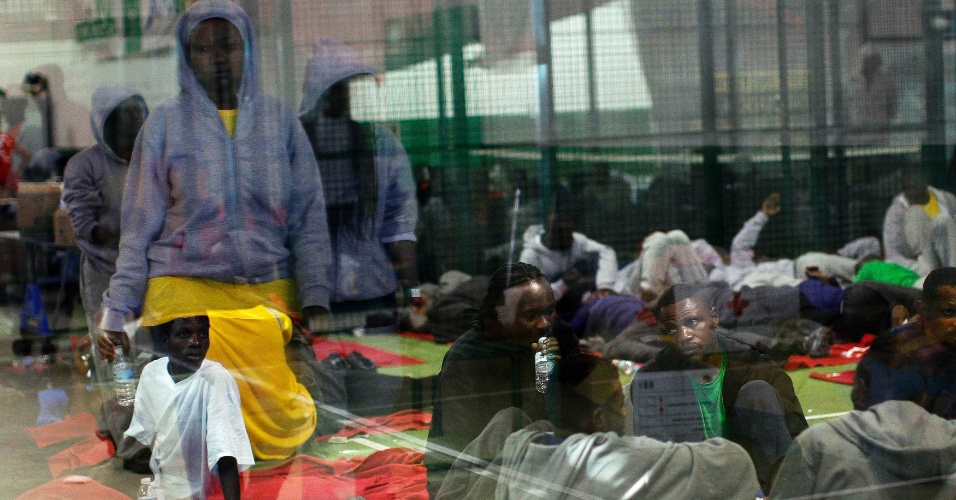 14.ago.2014 - Espelho reflete imagem de imigrantes em repouso dentro de um centro desportivo, após chegar em um navio de salvamento no porto de Tarifa, perto de Cadiz, na Espanha. A balsa em que viajavam afundou antes que eles fizessem a travessia para a Europa