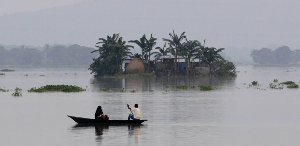 Indianos usam um barco para passar por casas parcialmente submersas no vilarejo de Balimukh, na Índia - Biju Boro/AFP