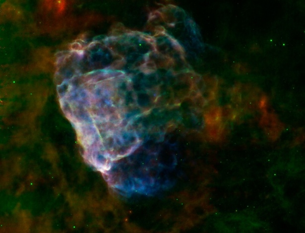 Imagem feita a partir de uma supernova captada pela Nasa e pela Agência Espacial Europeia mostra nuvem de poeira colorida. Informação em infravermelho do fotômetro de imagem do telescópio Spitzer, da Nasa, em ondas de 24 e 70 microns surgem em vermelho e verde e raios X do XMM-Newton em um alcance de 0.3 a 8 kiloelectron volts em azul - NASA/ESA/JPL-Caltech/GSFC/IAFE
