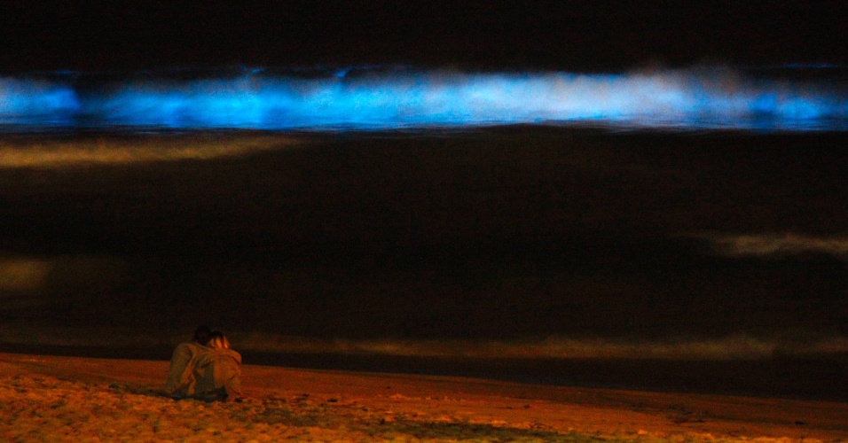 25.ago.2014 - Casal senta na areia da Praia de Manly à noite para assistir as ondas bioluminescentes azuis, em Sydney, na Austrália