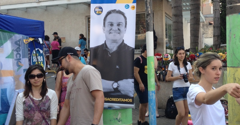 Visitantes da Feira da Vila Madalena passeiam entre barracas e propagandas políticas em rua do bairro paulistano