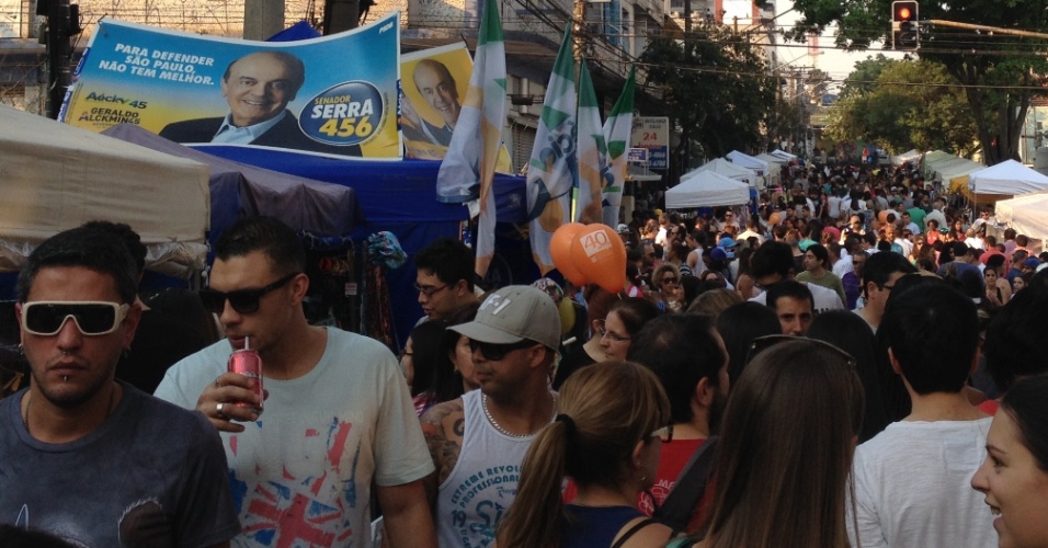 Visitantes da Feira da Vila Madalena passeiam entre barracas e propagandas políticas na rua do bairro paulistano