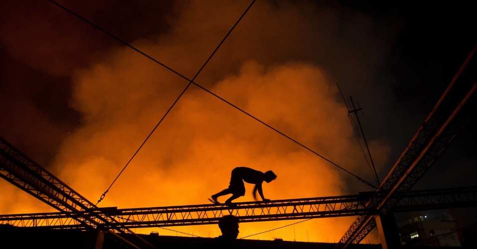 26.ago.2014 - Homem equilibra-se em estrutura de metal para atravessar de um edifício para outro durante um incêndio que tomou conta de armazém em Manila, nas Filipinas