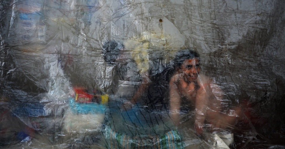 28.ago.2014 - Jovens se abrigam da chuva atrás de uma lona plástica em Nova Deli, na Índia