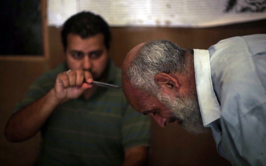 1º.set.2014 - Ibrahim Al Saied Sayeeh coloca uma abelha na cabeça de um homem que sofre de dores de cabeça e problemas de sinusite, no centro aberto por seu pai, Haj Saied Al Sayeeh, no Cairo (Egito). O pai de Ibrahim acredita que o veneno das abelhas tem propriedades especiais, que, quando utilizadas em partes específicas do corpo, pode curar doenças como problemas renais, apendicite e até câncer - Amr Abdallah Dalsh/Reuters