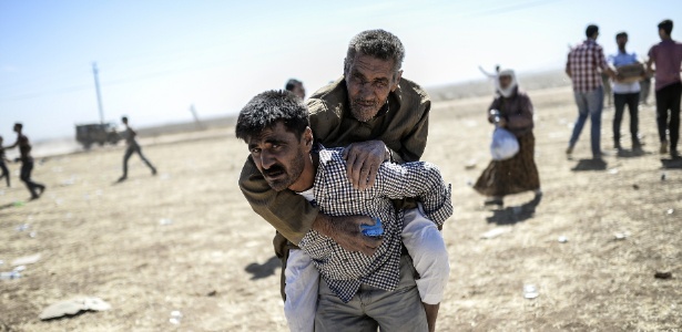 Homem curdo carrega idoso nas costas após cruzar a fronteira da Síria para a Turquia
