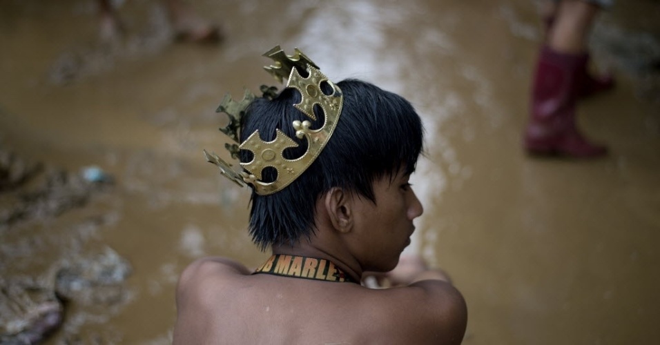 20.set.2014 - Rapaz usa coroa de plástico em beco coberto de lama na vila Banaba, no subúrbio de Manila, nas Filipinas, neste sábado (20), após fortes chuvas causadas pela tempestade tropical Fung-Wong