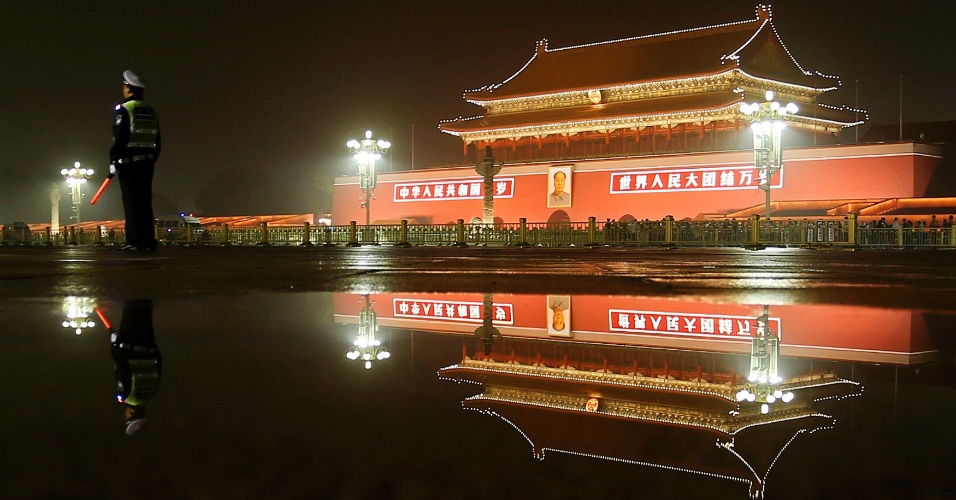 24.set.2014 - Policial e prédio da cidade proibída tem sua imagem refletida em poça d'água na praça Tiananmen, em Pequim, na China