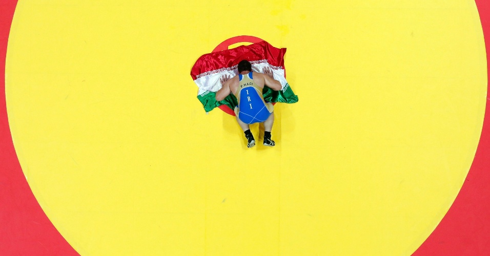 29.set.2014 - O atleta iraniano Parviz Hadi Basmanj resa em cima da bandeira do seu país após conquistar a medalha de ouro na luta greco-romana, durante os jogos asiáticos, em Incheon, na Coreia do Sul