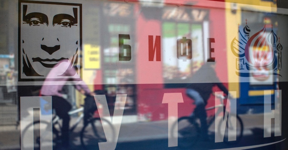 14.out.2014 - A imagem de ciclistas reflete na vitrine de um recém-inaugurado "Putin Bar" em Novi Sad, na Sérvia